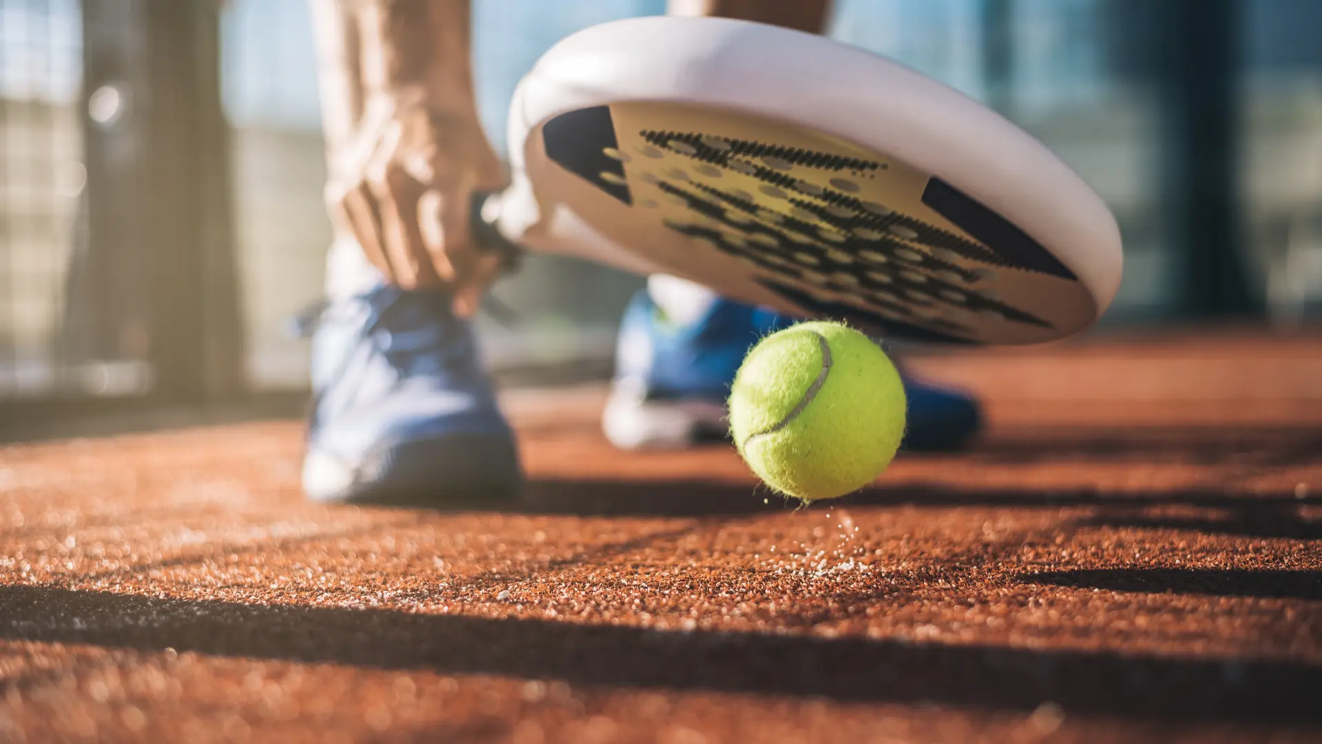 Raquette de padel et balle au ras du sol sur un court en terre battue